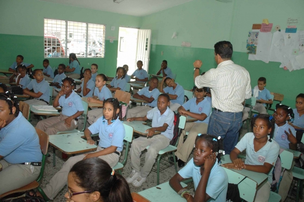 Niños y niñas de la educación básica, recibiendo instrucciones de su profesor en un aula de clases.