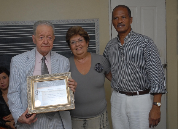 El maestro Rafael Bullomba Landestoy, exhibe su pergamino de reconocimiento entregado por el profesor Ivan Domínguez y la profesora Fárida Diná
