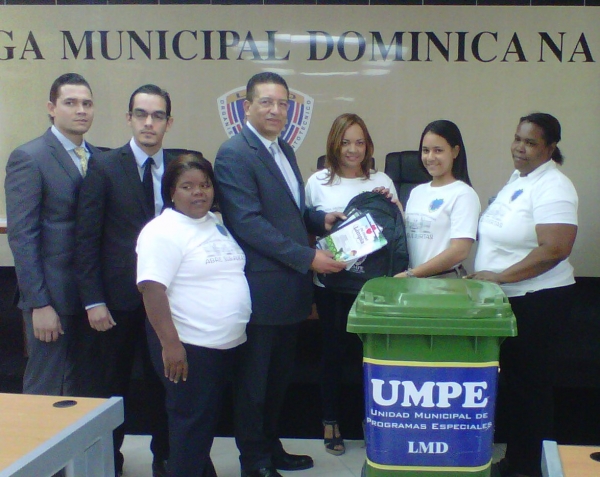Una de las profesoras del Liceo Fray Ramón Pane, recibe en nombre de los estudiantes los útiles escolares y los contenedores de parte del secreetario general de la Liga Municipal Dominicana, Johnny Jones