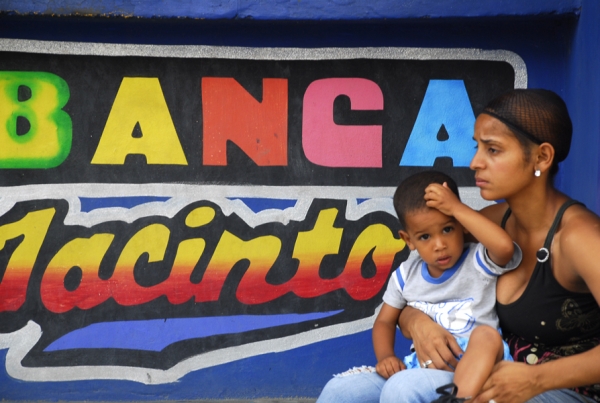 Una mujer joven, carga su niño, mientras atiende una banca de lotería, por la falta de oportunidades que tiene la juventud.