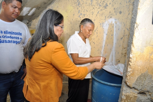 La ministra de trabajo, Maritza Hernández, explica a uno de las residentes de los sectores del operativo como se elimina los criaderos de mosquitos