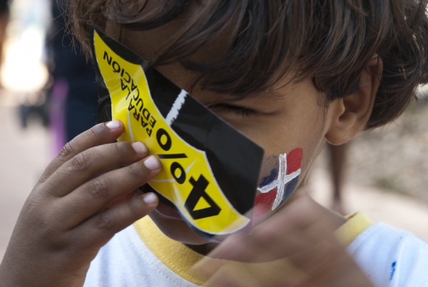 Niño se cubre la cara con una etiqueta de la campaña exigiendo el 4% para la educación.